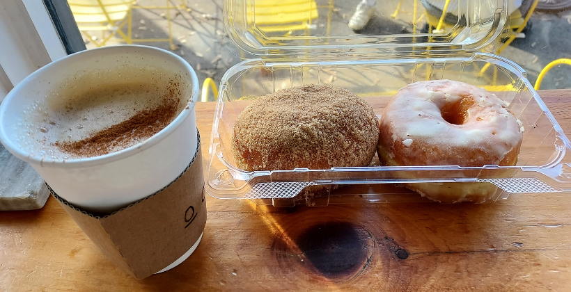 How to start a coffee business. One to go cup of chai on the left and two brioche donuts in a plastic to-go container on the right.