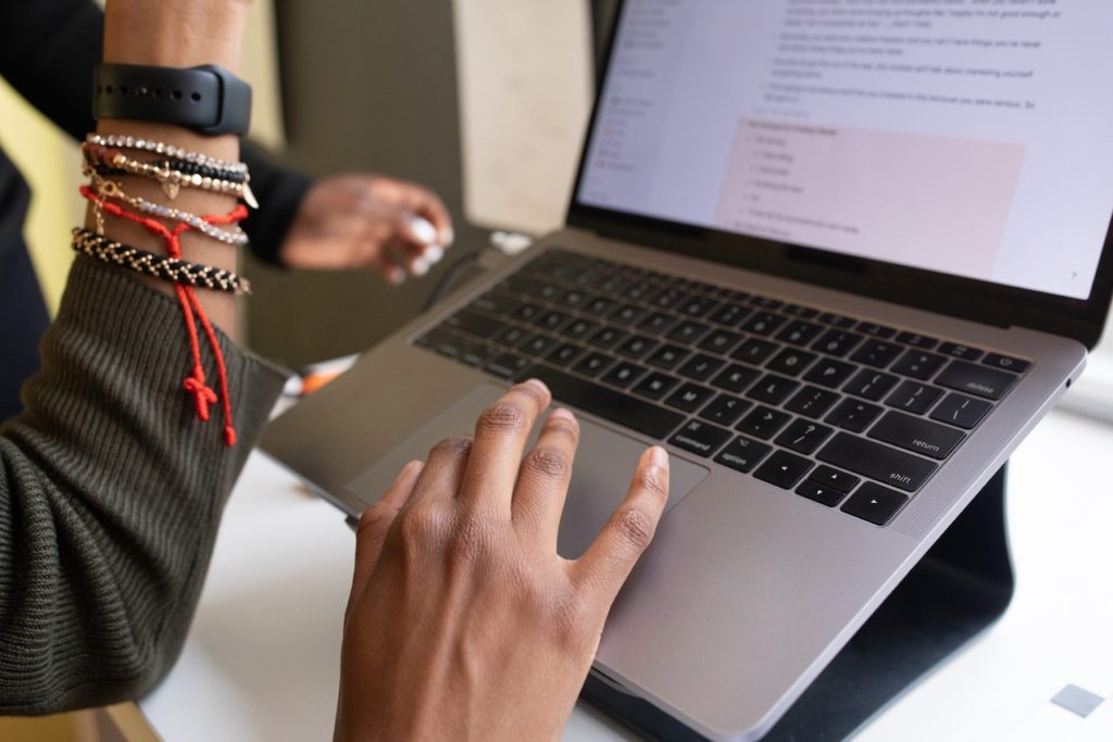 Small business funding. Woman on a Macbook computer with a black watch and bracelets on her left arm.