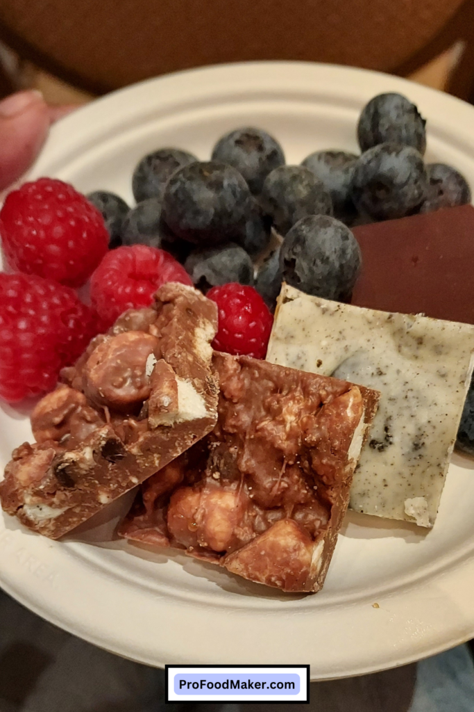 Close up shot of snacks: fresh blueberries & raspberries, then an assortment of chocolate bark, some with oreo and white chocolate, and some with nuts