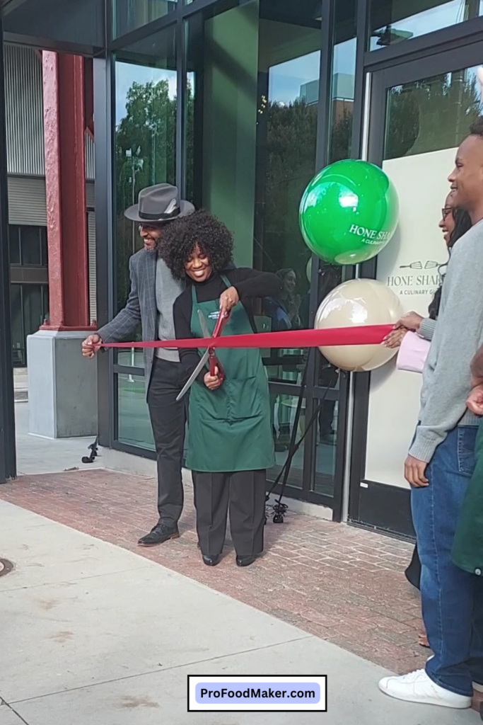 Cherisse Byers stands in front of Hone Sharpen with large scissors before cutting the ribbon next to her husband, Mike.