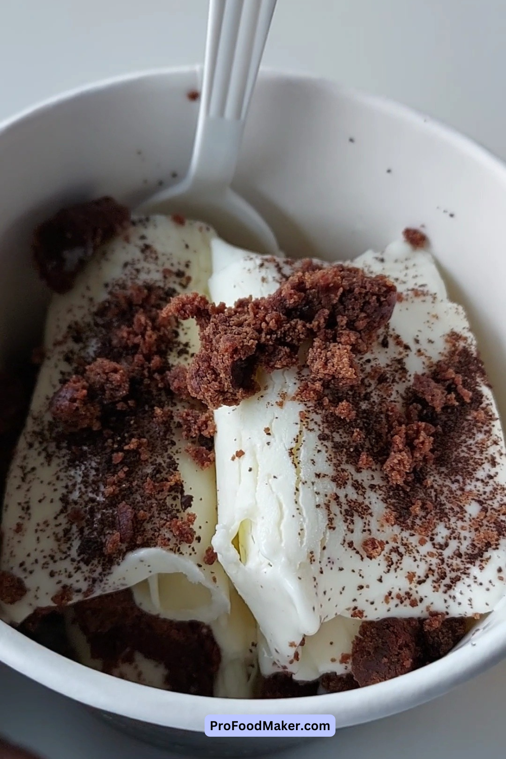 Vanilla ice cream with brownie pieces in a plastic white bowl and spoon.