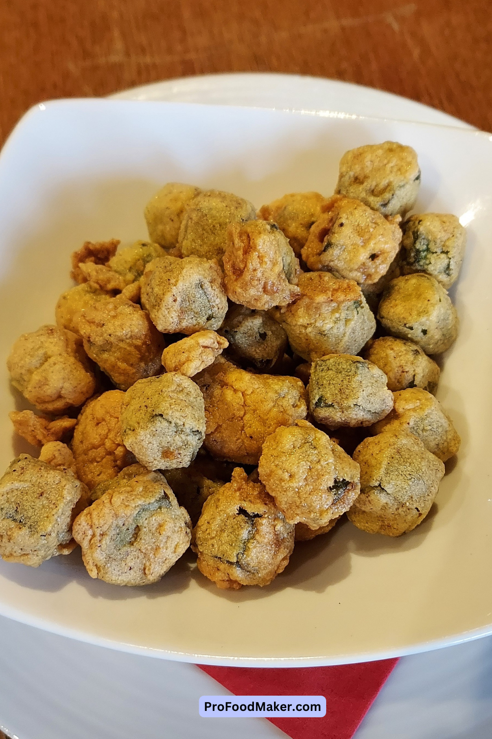Fried okra in a white rounded rectangular bowl on top of a red napkin
