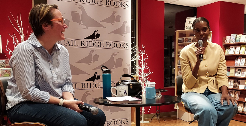 Spring Council sits in a chair with a microphone being interviewed at Quail Ridge Books