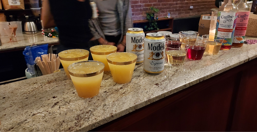 Drinks made with Modelo and/or Caribe & Co Caribbean-inspired syrups. Several drinks in small plastic cups sit on a bar counter at Padmore's in Brooklyn.