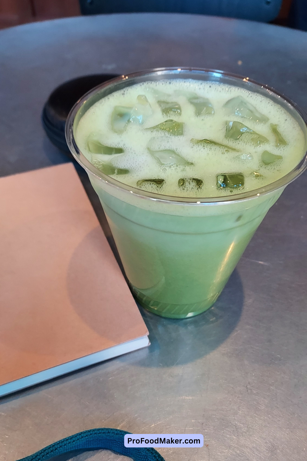 Iced matcha latte from Padmore's Brooklyn. The drink is in a clear plastic cup on a table next to a small notebook. 