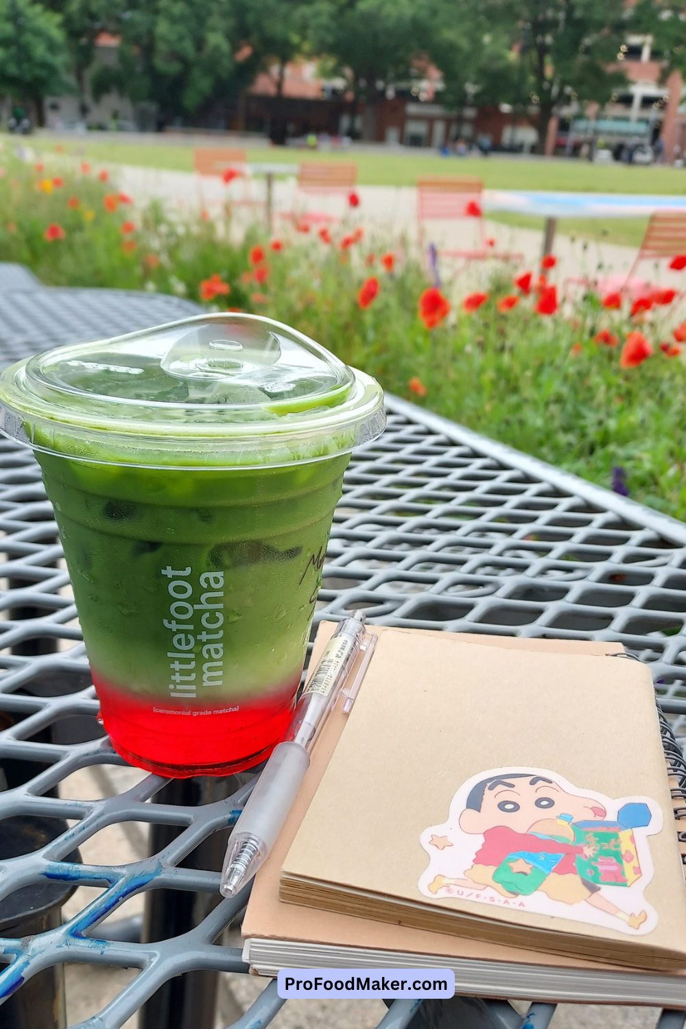 strawberry matcha latte next to two notebooks surrounded by a field of red flowers